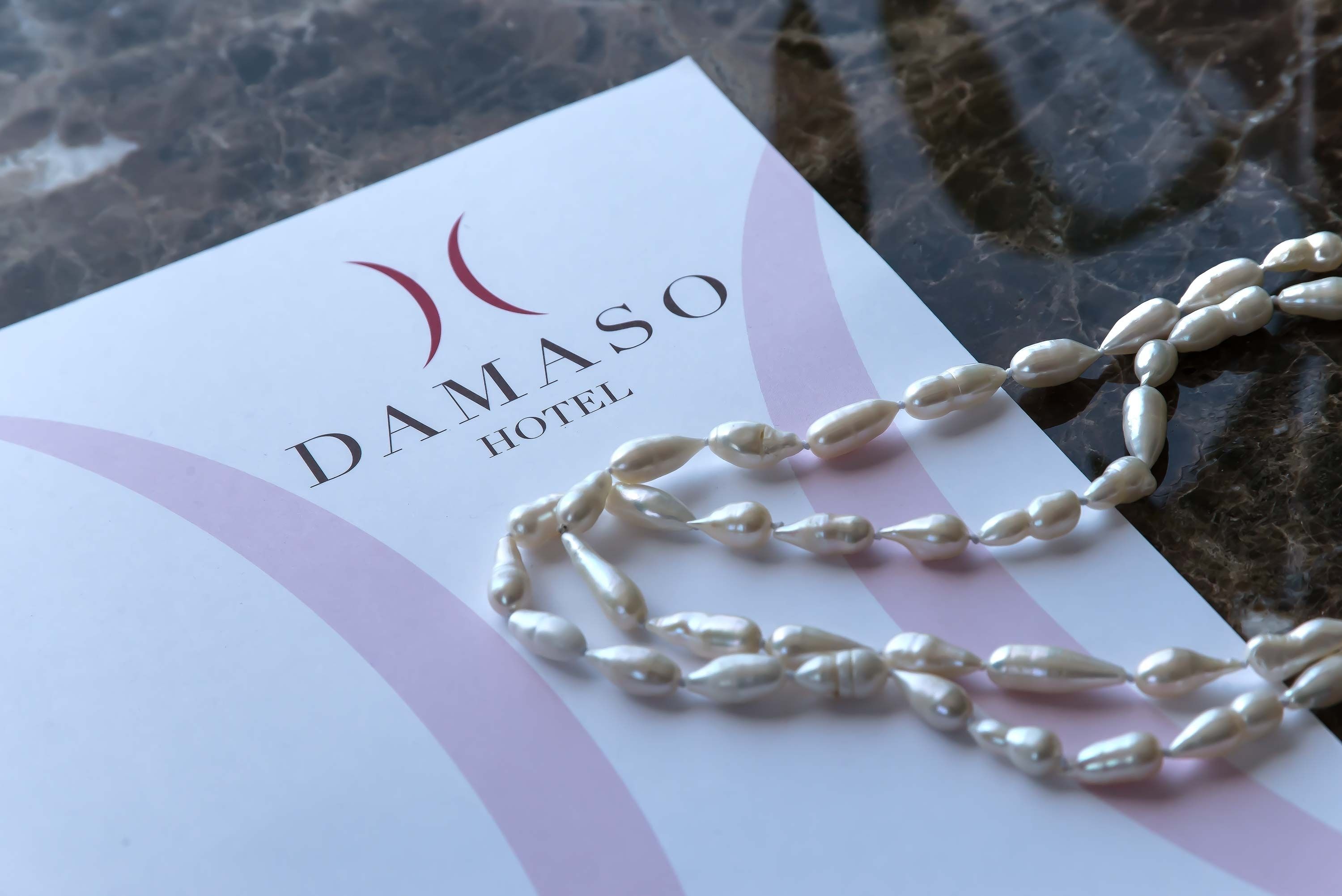 A DAMASO HOTEL business card with a pearl necklace on top.