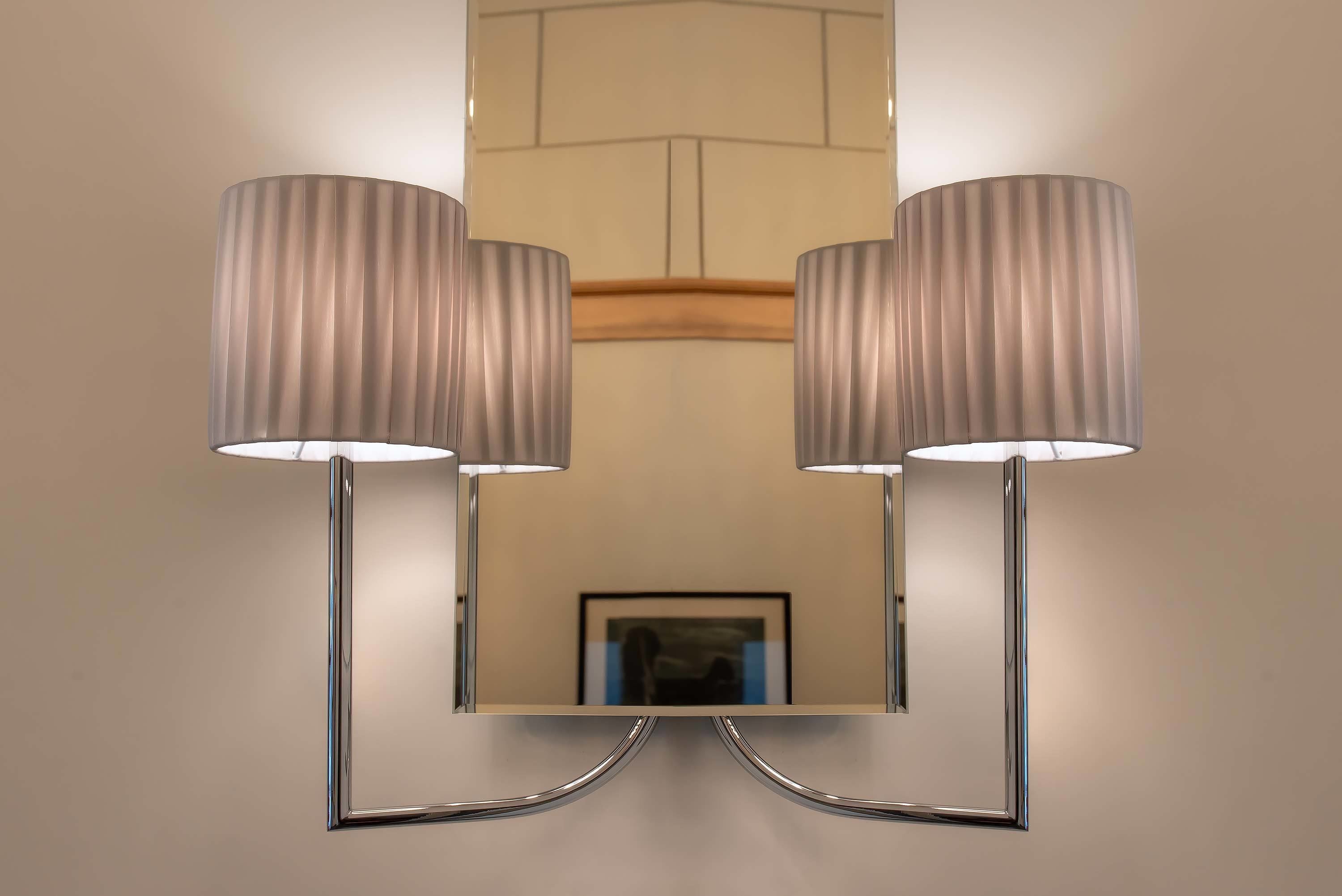Een muurlamp met twee cilindrische lampenkappen en een chromen voet.