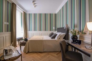A hotel room with a bed, bedside table, chair, and a desk with a lamp.