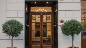 A hotel entrance with a wooden double door, a chandelier above, and a doormat with the hotel's name. - Damaso Hotel (Rome)