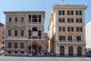 A historic building with a classical facade, a prominent entrance with a sign, and a balcony on the second floor.