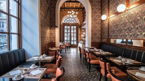 A restaurant with booths and tables, a patterned wall, and a large arched window. - Damaso Hotel (Rome)