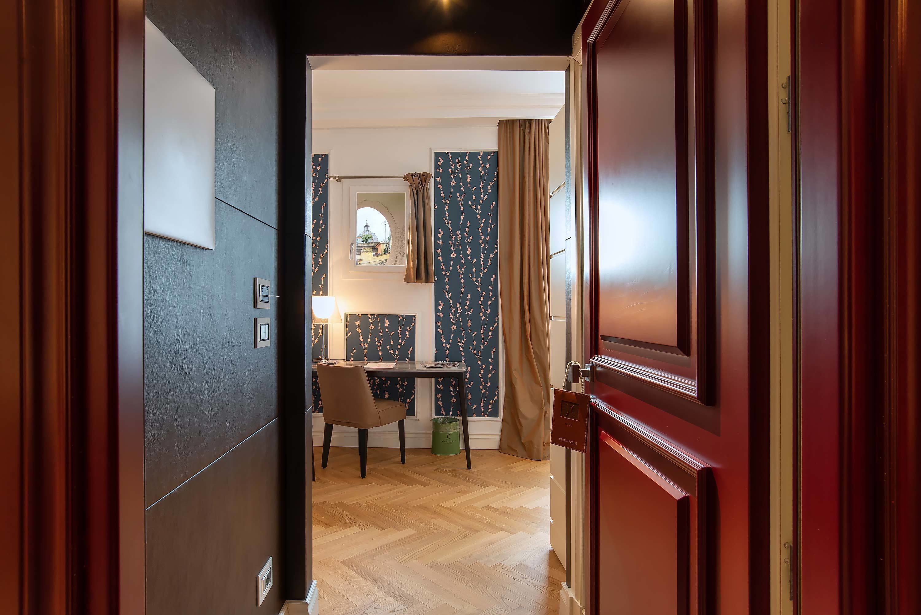 A hallway with a desk, chair, and a view through a window.