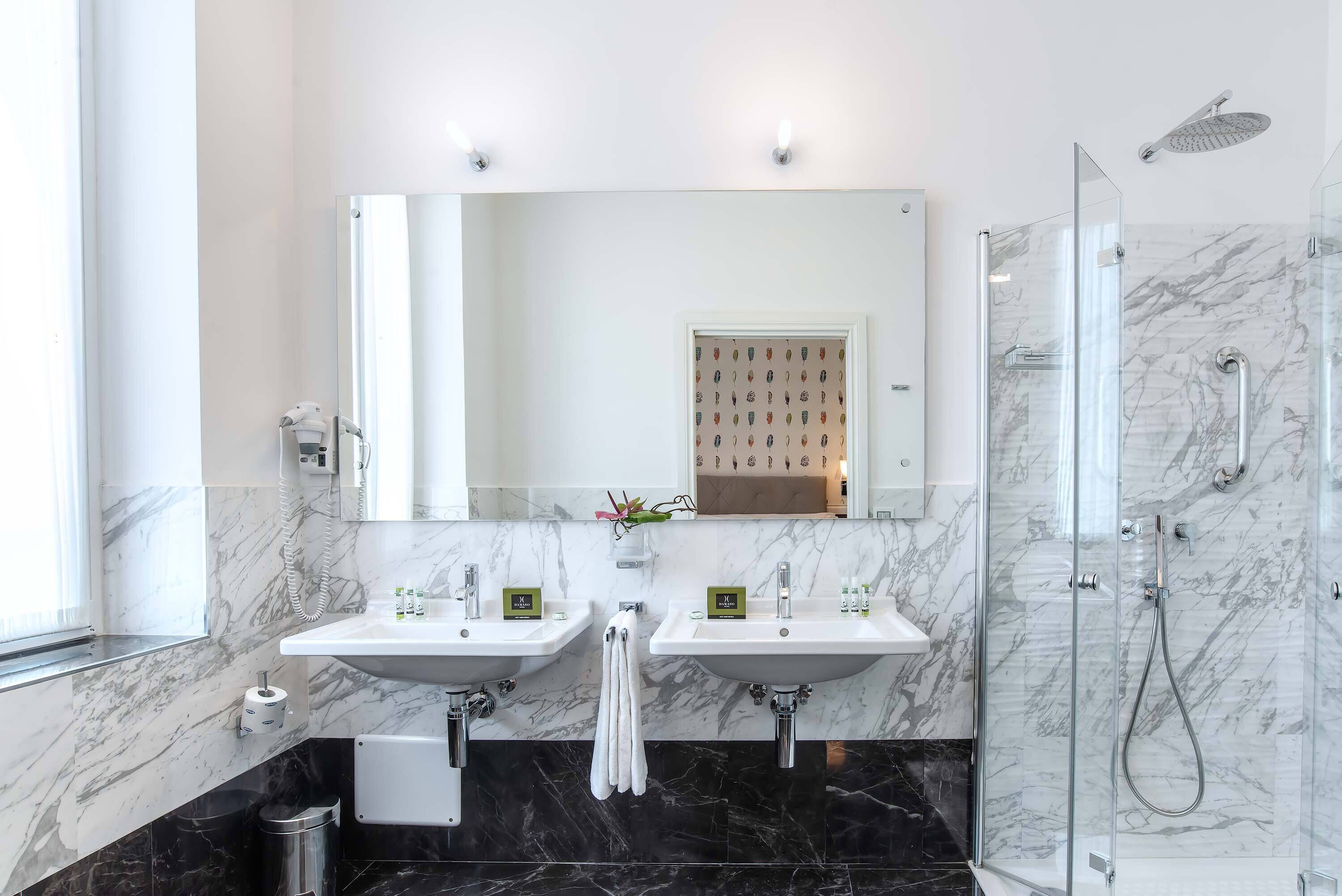 Un baño moderno con dos lavamanos, un espejo grande, cabina de ducha con paredes de vidrio y piso de mármol.