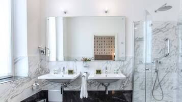 Un baño moderno con dos lavamanos, un espejo grande, cabina de ducha con paredes de vidrio y piso de mármol.