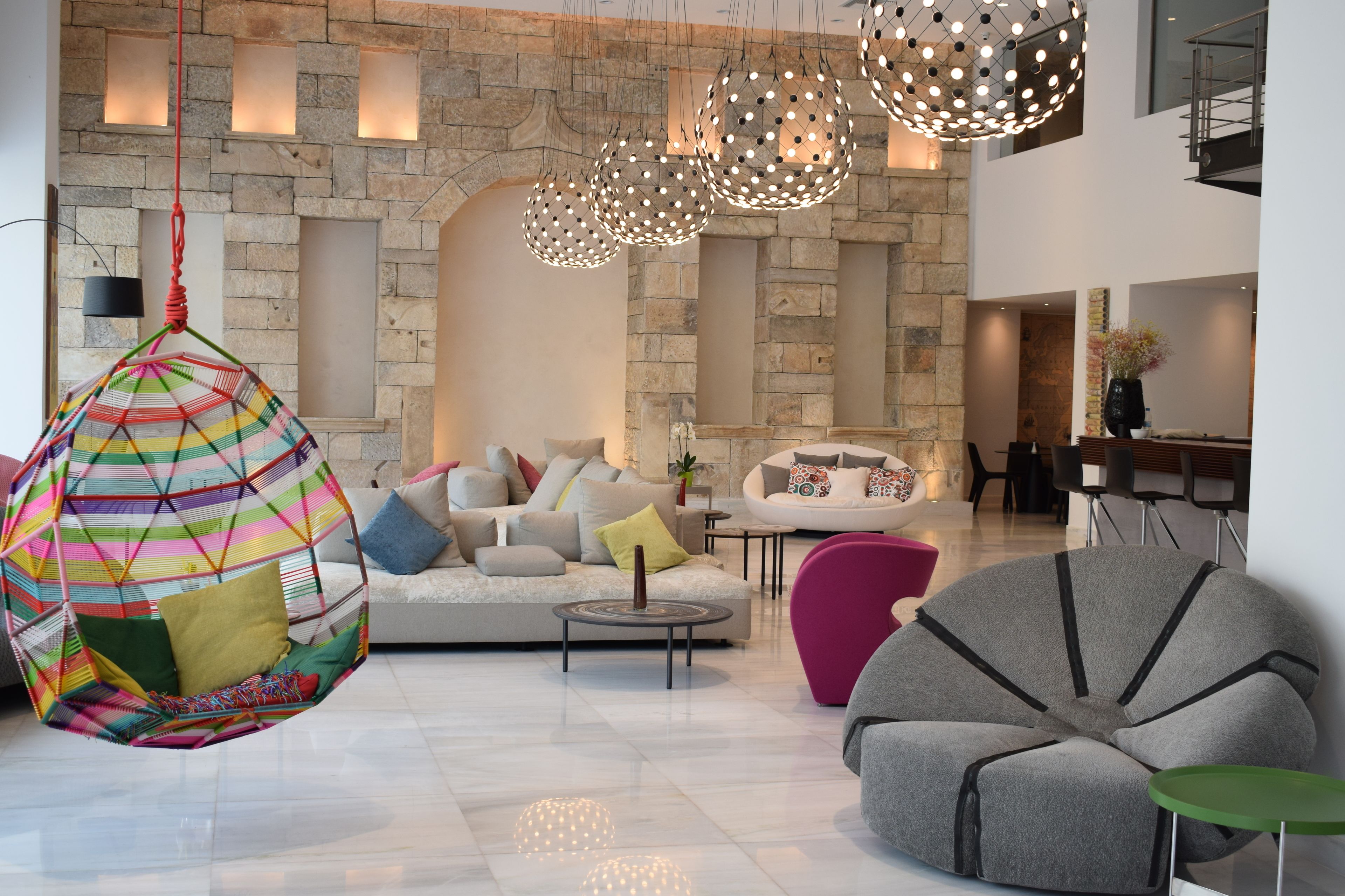 A modern living room with a stone wall, a hanging chair, a grey armchair, and a round table.