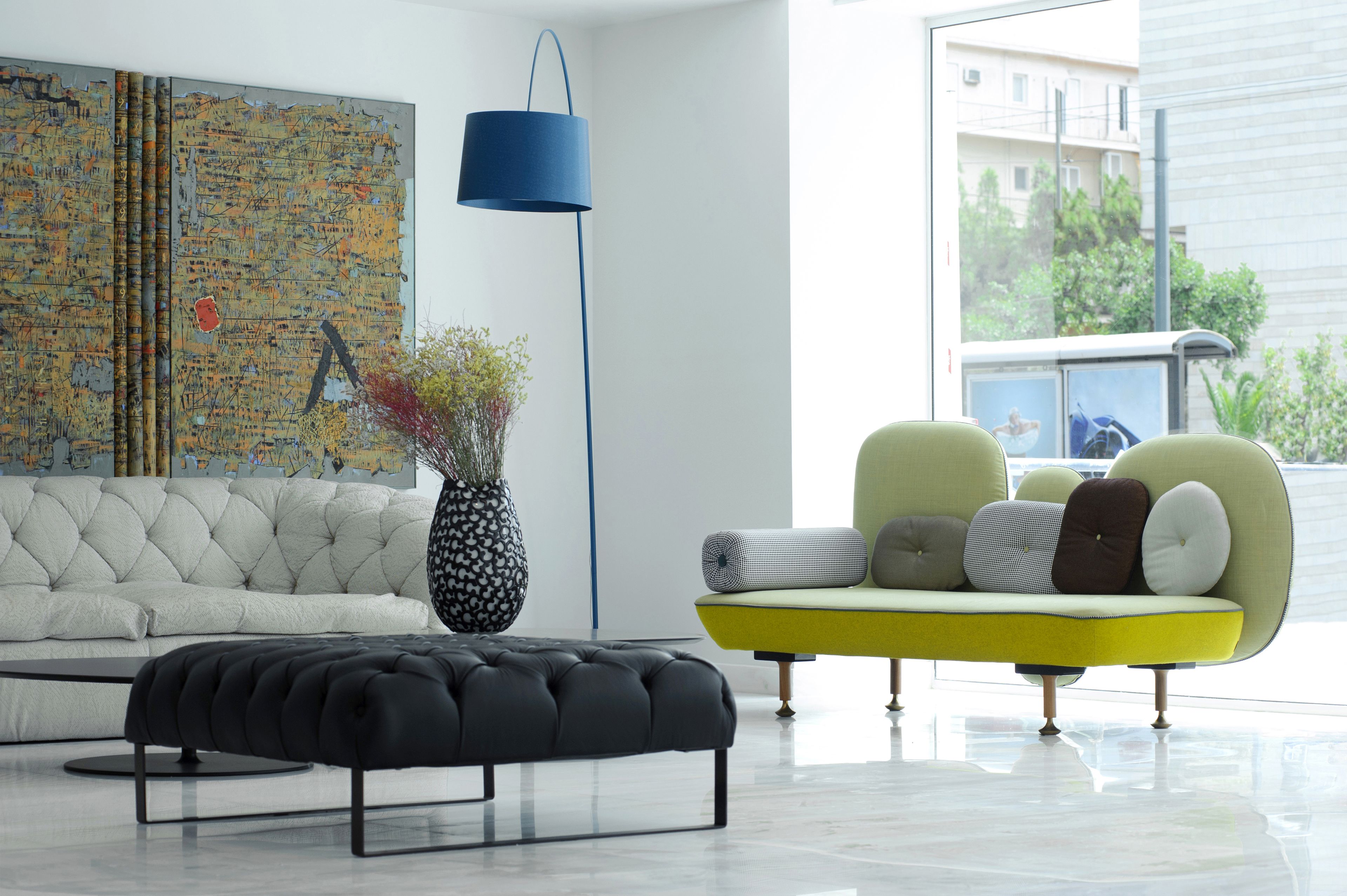 Un salón moderno con un sofá blanco, un sillón amarillo, un reposapiés negro y un cuadro abstracto grande en la pared.