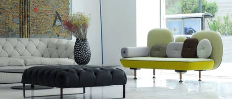 Un salón moderno con un sofá blanco, un sillón amarillo, un reposapiés negro y un cuadro abstracto grande en la pared.