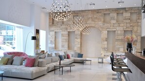 A modern living area with a stone wall, a sofa set, and a bar area. - Athenaeum Grand Hotel (Kallithea)