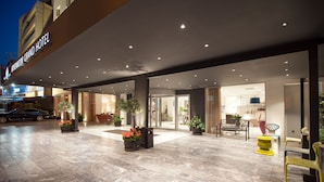 A hotel entrance with a covered outdoor area, potted plants, and seating. - Athenaeum Grand Hotel (Kallithea)