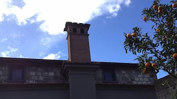Un edificio in pietra con un camino e un albero carico d'arance.