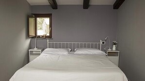 Un dormitorio con cama, mesitas de noche, ventana y lámpara.