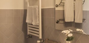 A bathroom with a towel rack, a mirror, and a potted plant with white flowers. - Podere don Peppe 1884 (Massa Lubrense)