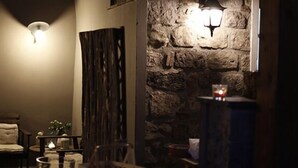 Una habitación acogedora con pared de piedra, chimenea, una silla y una pequeña mesa con una vela.