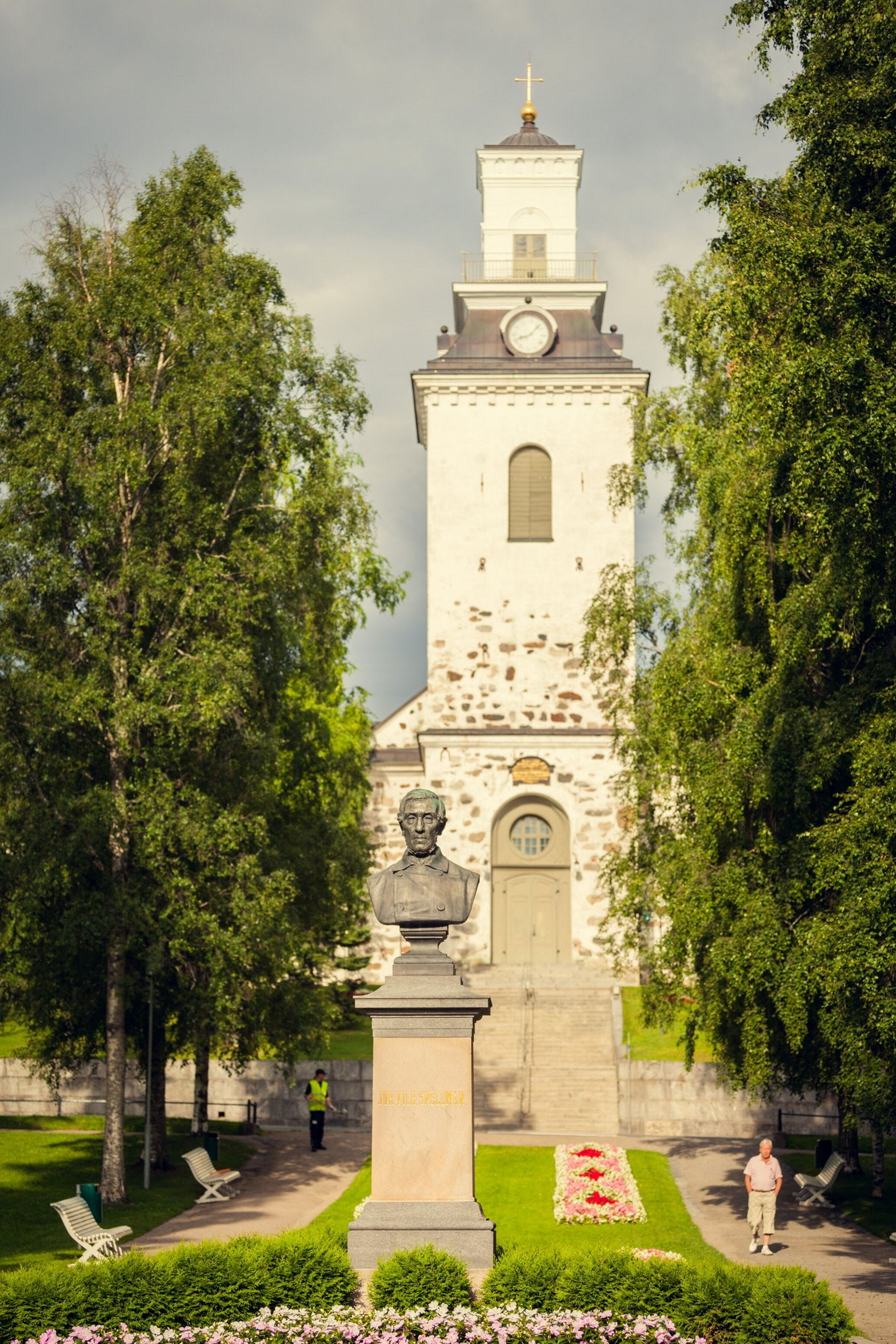 A church with a bell tower, a statue in front, and a well-maintained garden.
