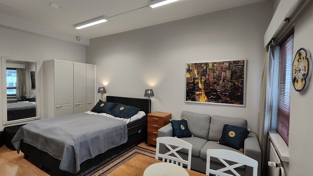Een slaapkamer met een bed, een dressoir, een nachtkastje, een bank en een stadslandschap schilderij.