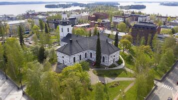 An aerial view of a cityscape with a prominent white church with a black roof, surrounded by green trees and buildings.