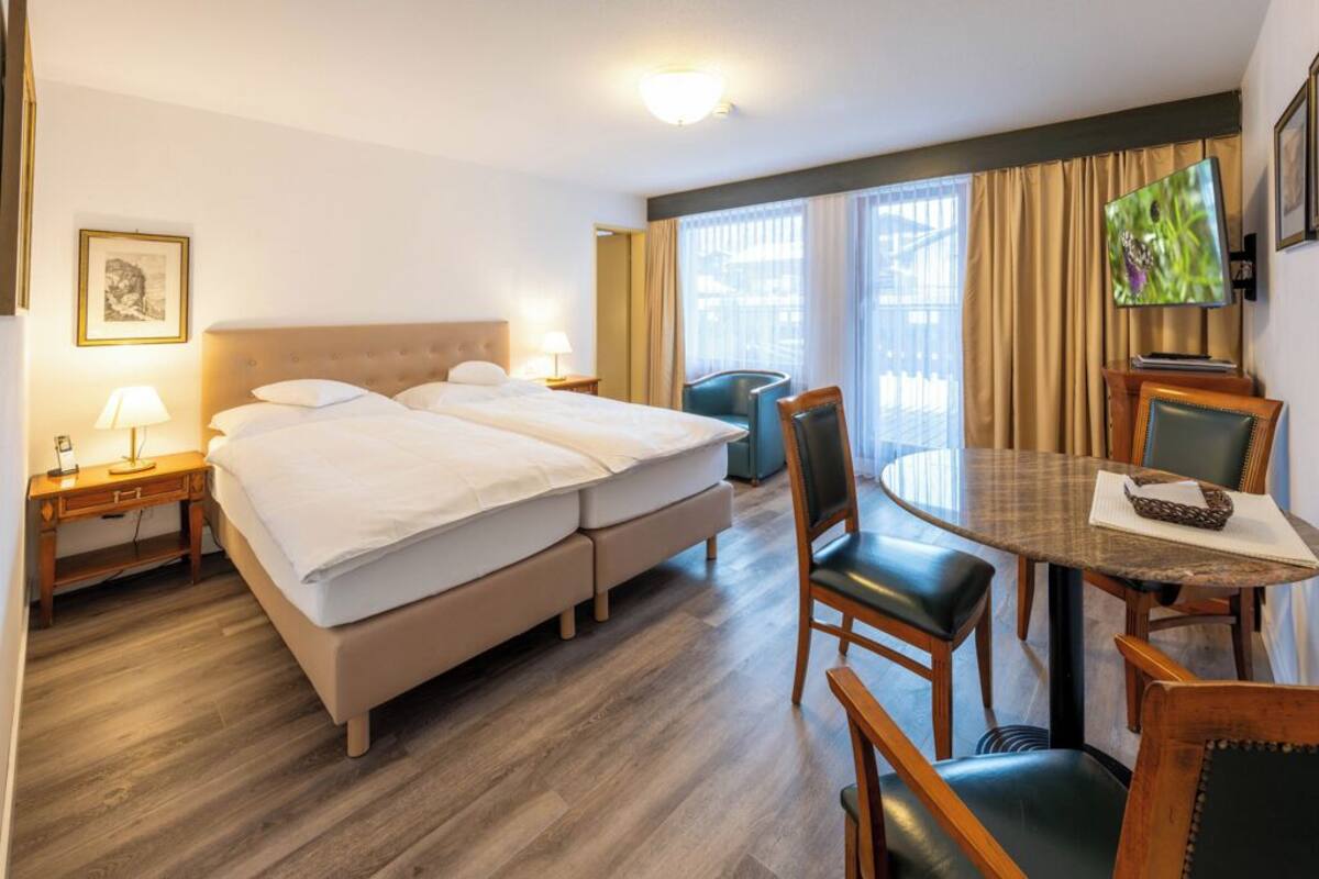 A hotel room with a double bed, a desk with a chair, a television, and a window with curtains.