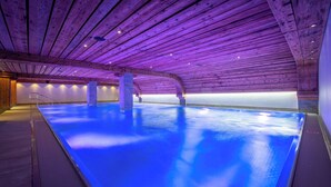 An indoor swimming pool with a wooden ceiling and a blue-lit floor. - Arca Aparthotel & Spa (Zermatt)