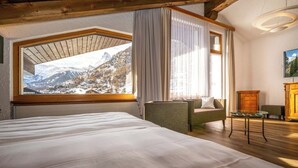 A bedroom with a large bed, a view of mountains through a window, and a wooden ceiling. - Arca Aparthotel & Spa (Zermatt)