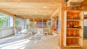 A spacious room with a wooden ceiling, large windows, and a wooden bookshelf. - Arca Aparthotel & Spa (Zermatt)