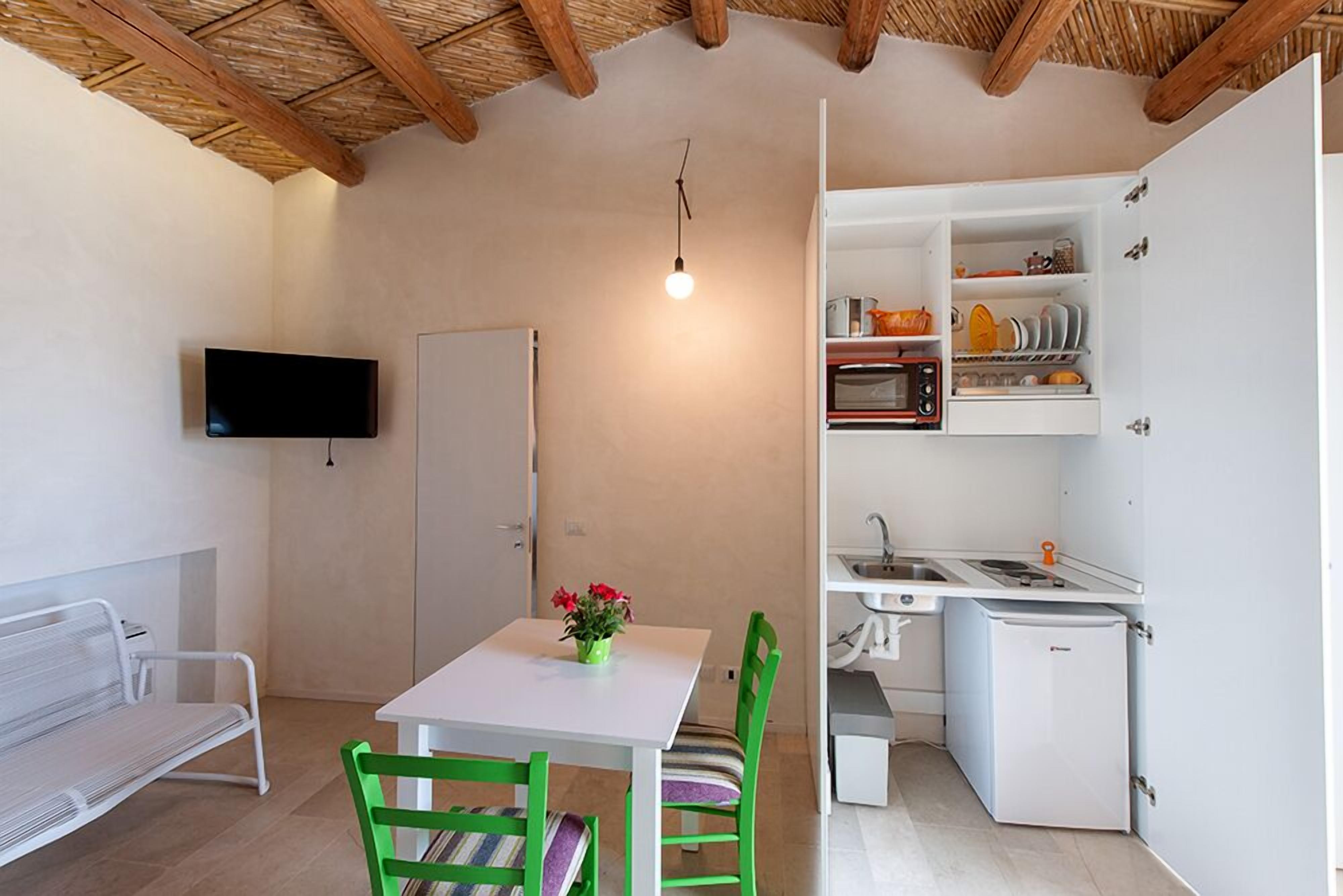 Una cocina compacta con horno integrado, un lavamanos y un refrigerador. Hay un comedor con una mesa y sillas, y un televisor montado en la pared.