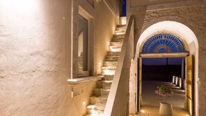 Un escalier en pierre mène à une porte en arc surmontée d’un fanal décoratif bleu.