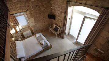 A bedroom with a stone wall, a bed, a small table, a chair, and a TV mounted on the wall.