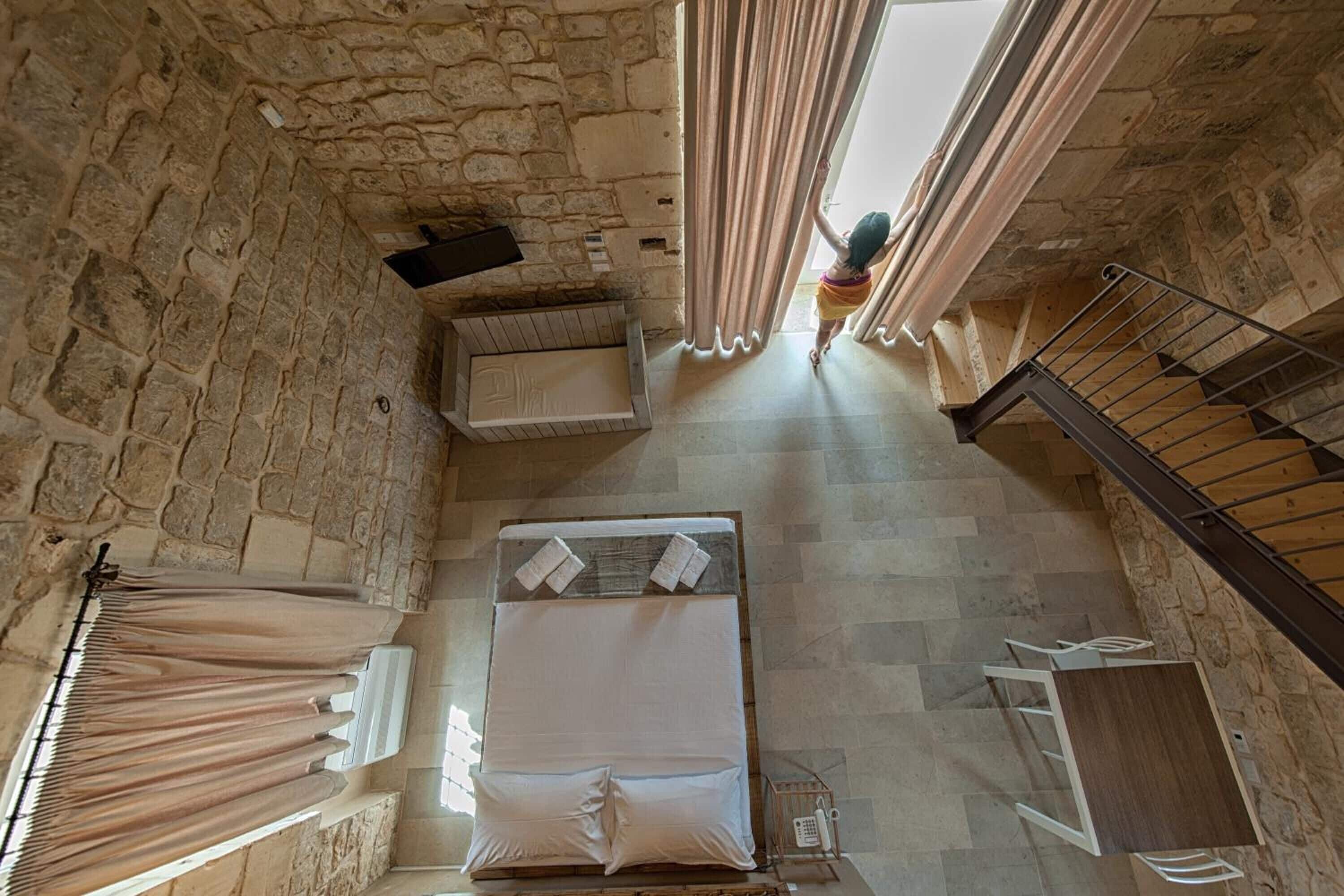 Una habitación con techos altos y paredes de piedra, con una cama, una mesita y una escalera.