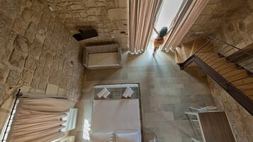 Una habitación con techos altos y paredes de piedra, con una cama, una mesita y una escalera.
