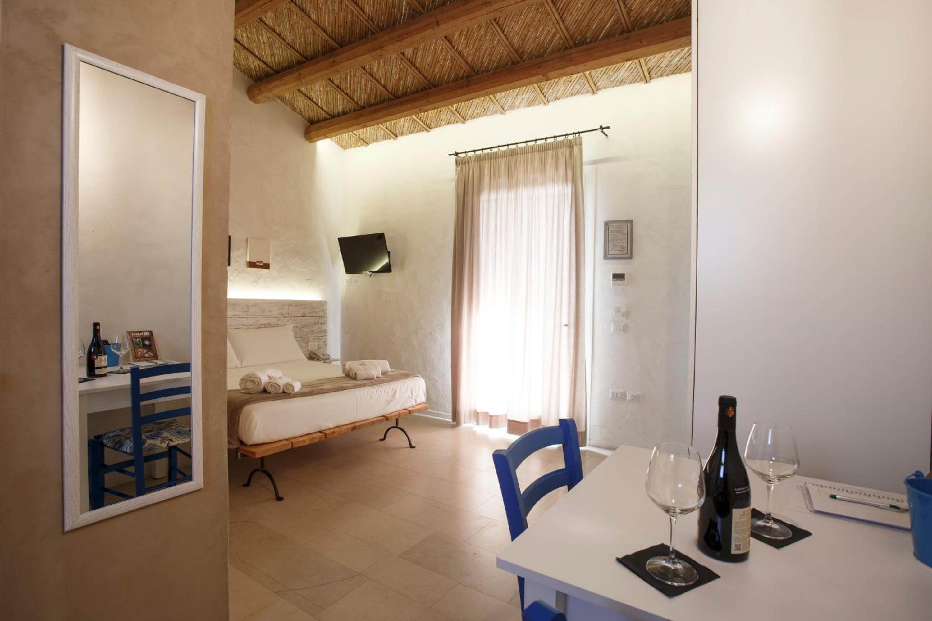 A room with a bed, a table with wine glasses and a bottle, a chair, and a TV mounted on the wall.