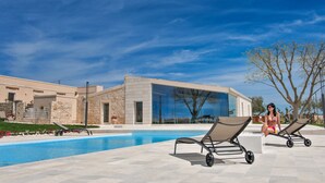 Un espace piscine moderne avec des chaises longues et un ciel d’un bleu éclatant.