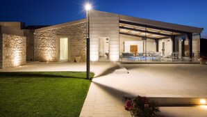 Une maison moderne avec une façade en pierre, un espace extérieur couvert et une allée bien éclairée.
