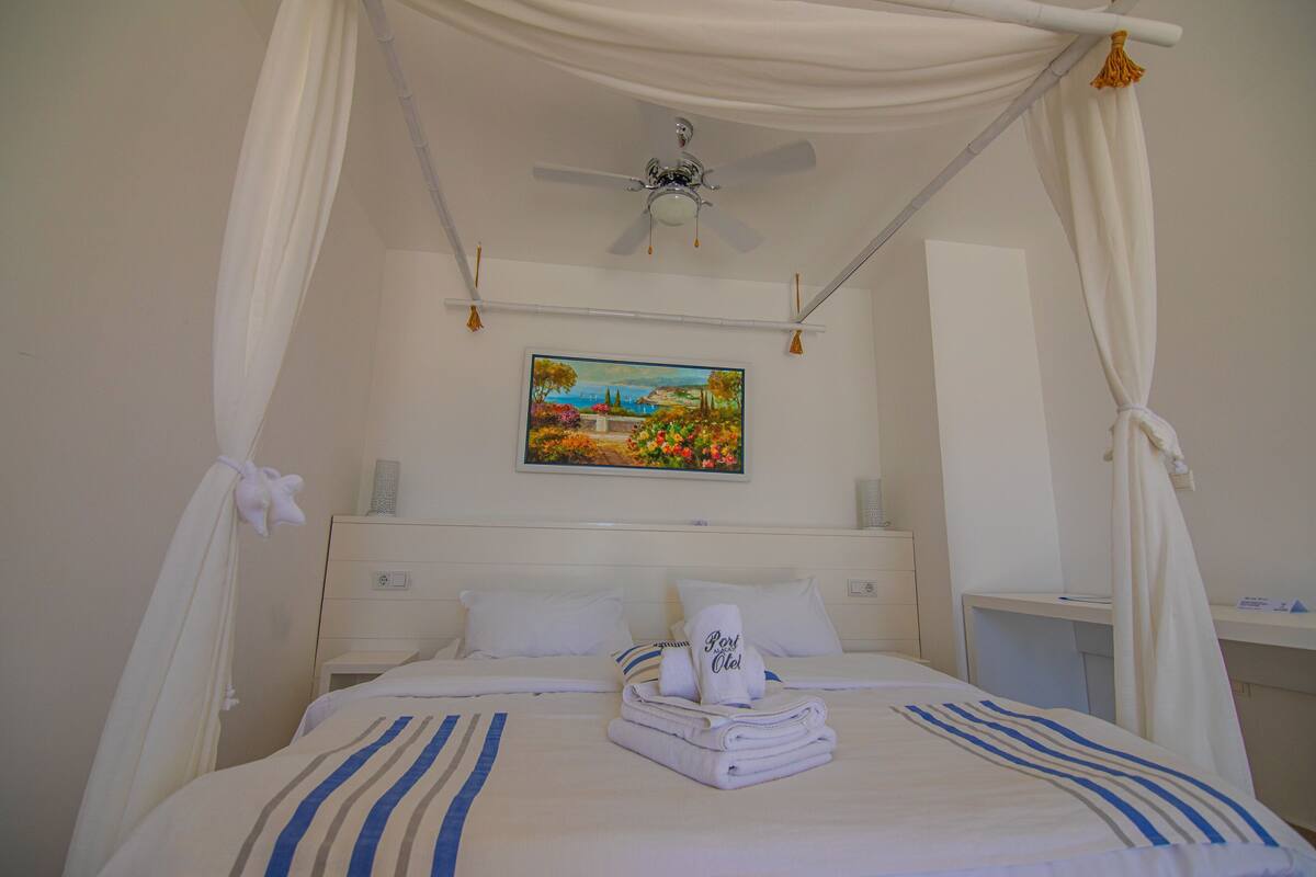 A neatly made bed with a canopy, a painting on the wall, and a bedside table.