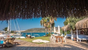 A wooden deck with lounge chairs and tables, overlooking a marina with boats and a clear blue sea. - Port Alacati Hotel (Cesme)