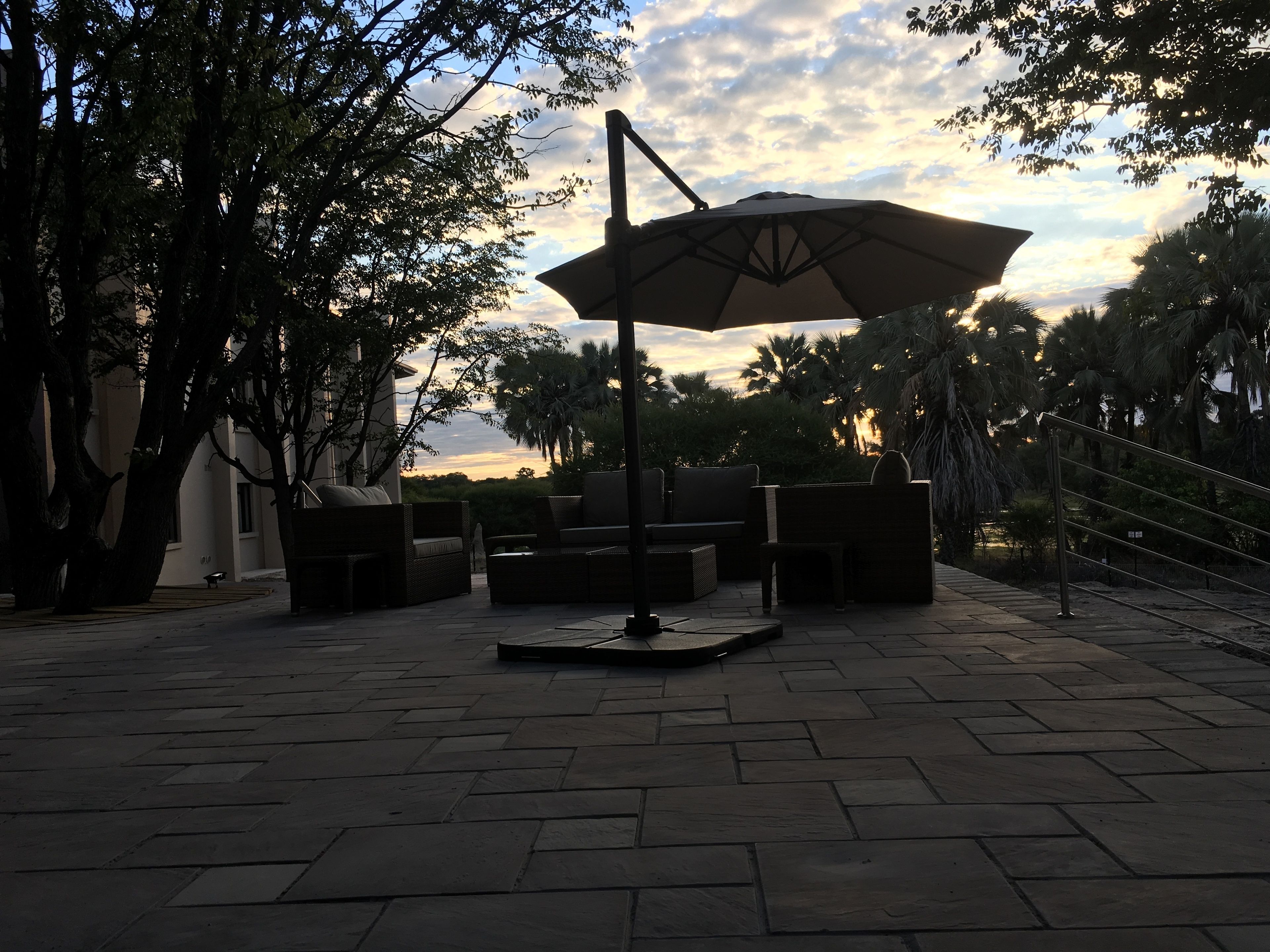 An outdoor patio area with a large umbrella, wicker furniture, and a paved walkway.