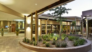A hotel lobby with a reception desk, seating area, and a garden with plants and a tree. - Cresta Maun (Maun)
