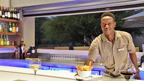 A bar area with a bartender, a wine glass, and a bowl of fries. - Cresta Maun (Maun)