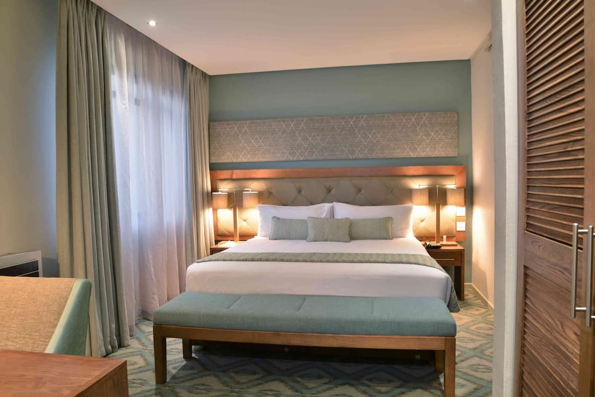 Una habitación de hotel con una cama grande, lámparas de noche, un banco de madera y una alfombra estampada.