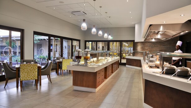 A modern restaurant with a central island, seating area, and a kitchen visible. - Cresta Maun (Maun)
