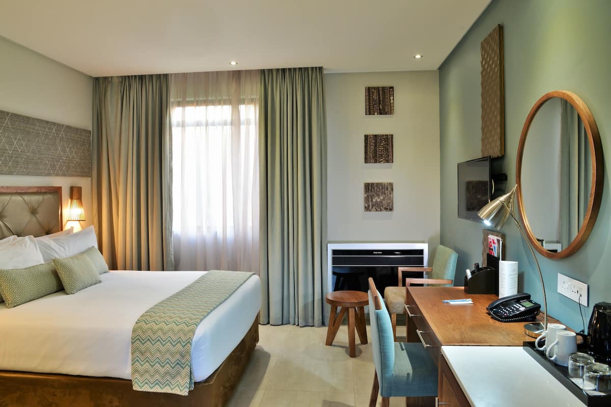 Una habitación de hotel con una cama grande, un escritorio con silla, un televisor y un espejo.