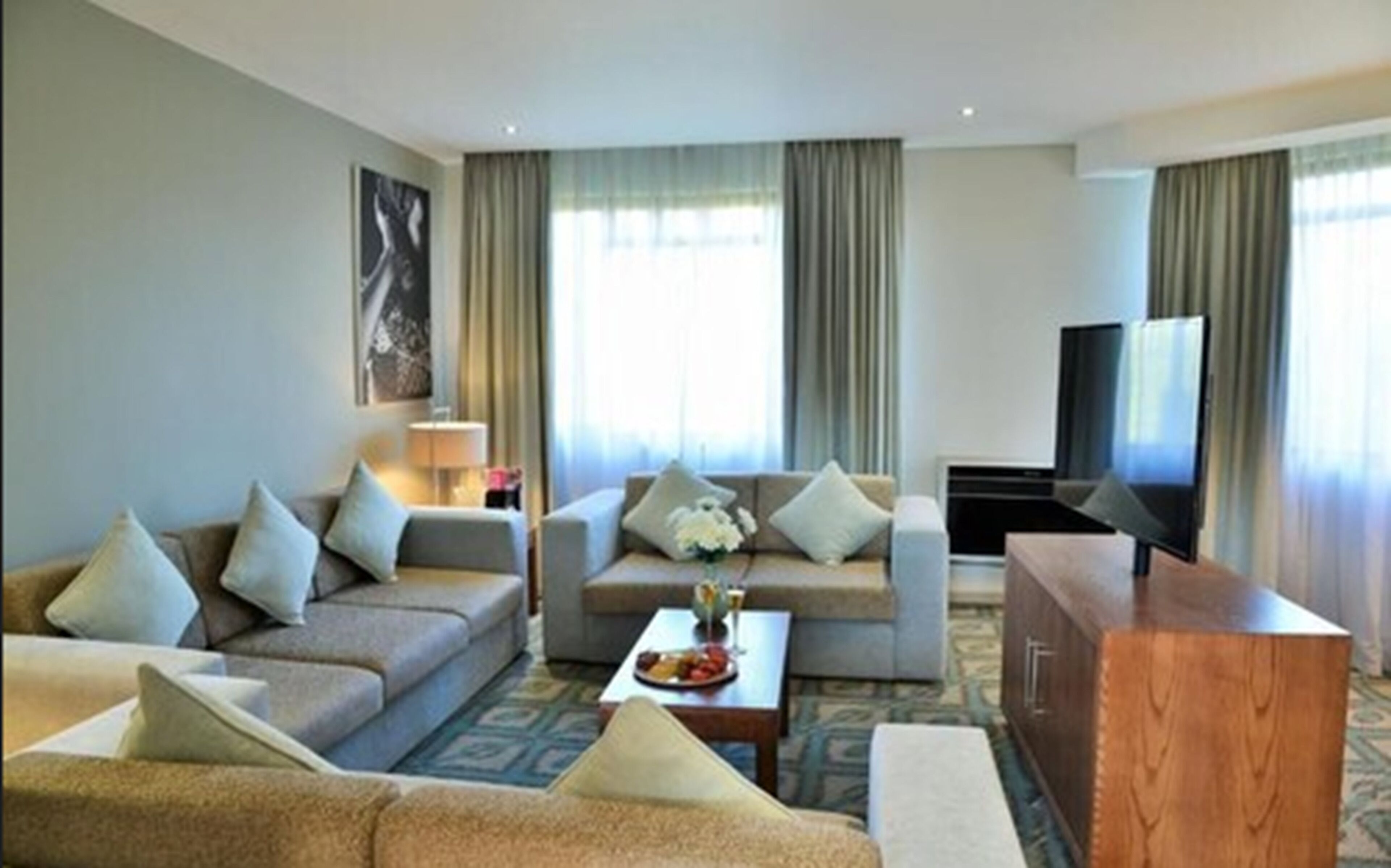 A modern hotel room with a sofa set, a coffee table, a TV, and a cabinet.