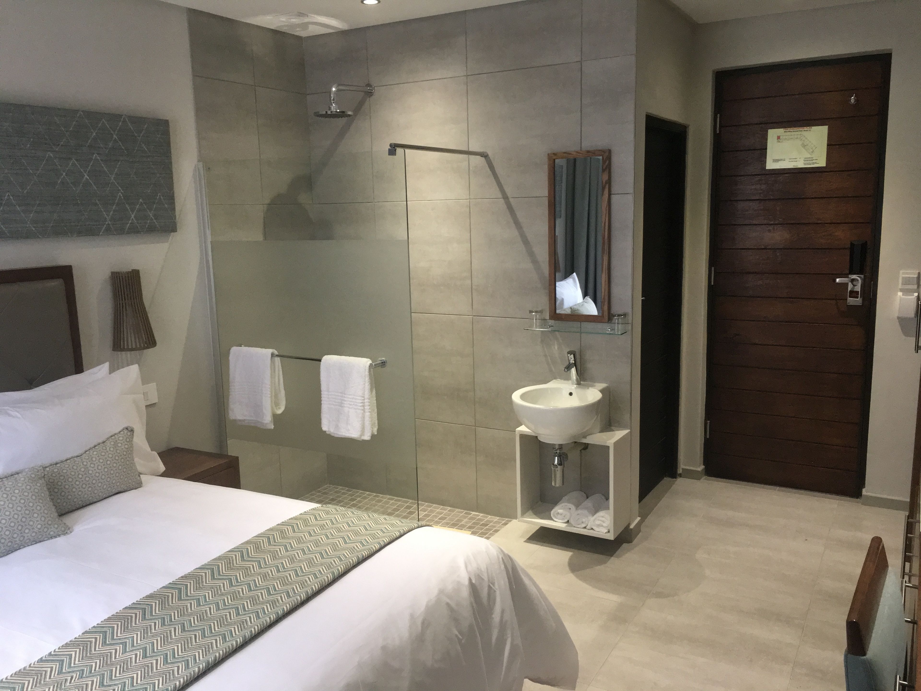 A modern hotel room with a large bed, a bathroom with a sink and mirror, and a wooden door.
