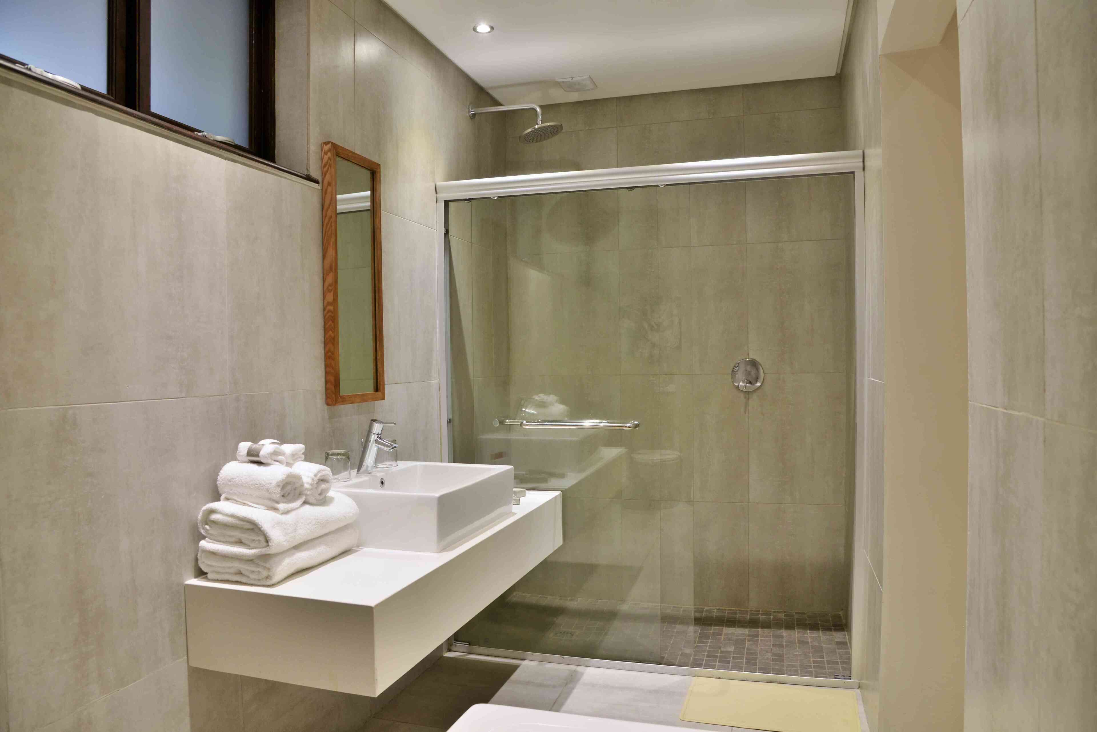 A modern bathroom with a glass-enclosed shower, a white sink, and a mirror.
