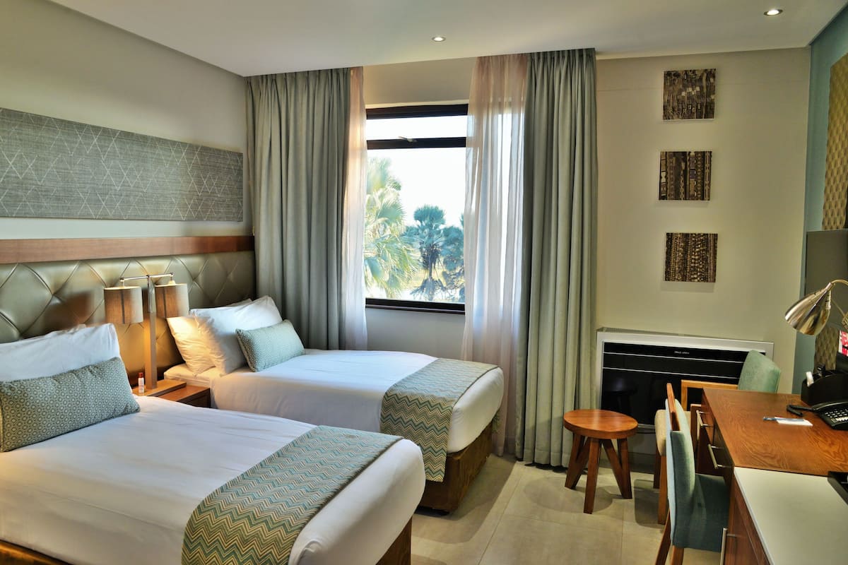 Habitación de hotel con dos camas, un escritorio, una silla, un televisor y una ventana con cortinas.