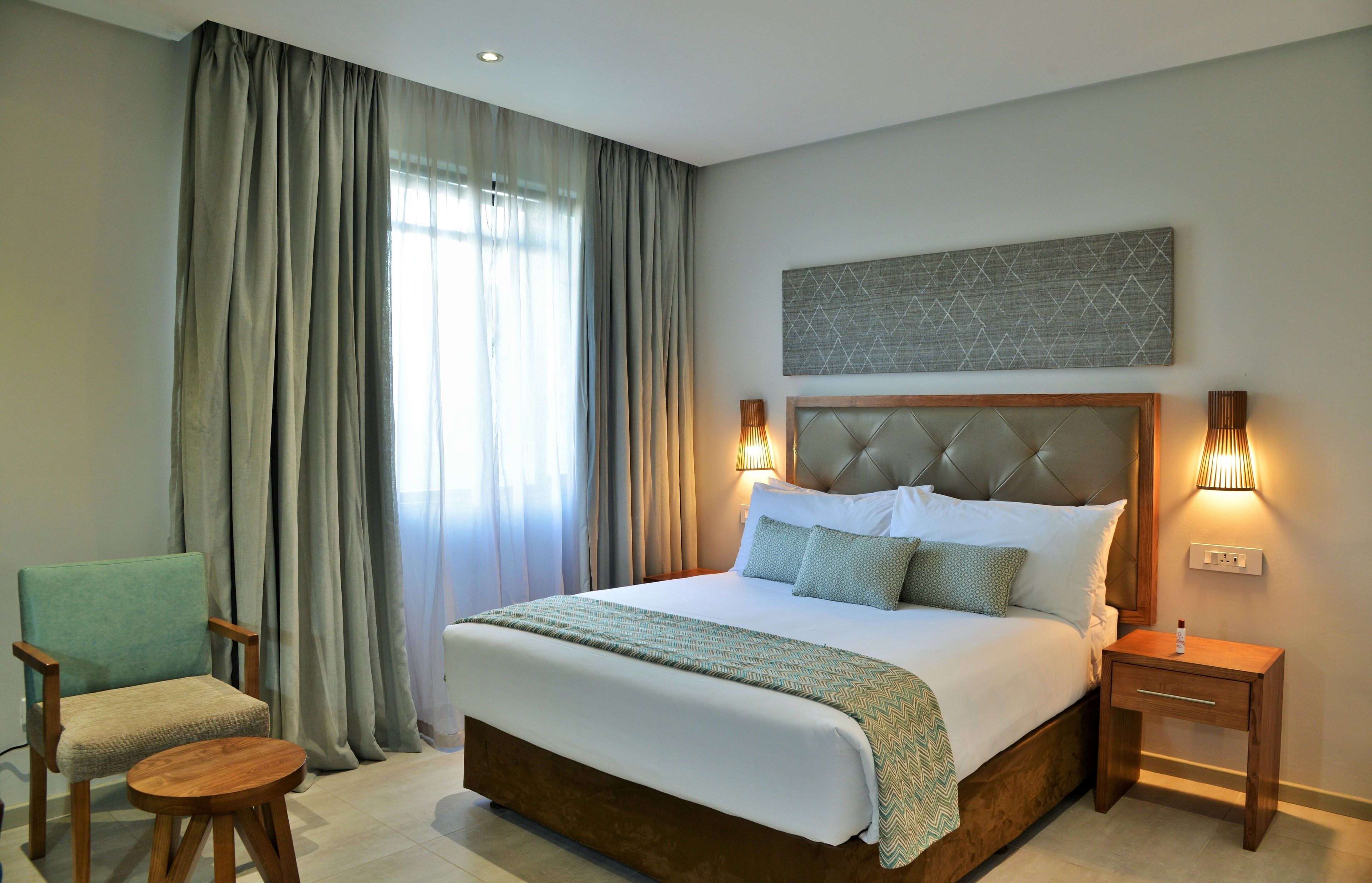 A hotel room with a large bed, a chair, a bedside table, and a lamp.