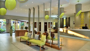 A reception area with a reception desk, seating area with chairs and cushions, and a large potted plant. - Cresta Maun (Maun)
