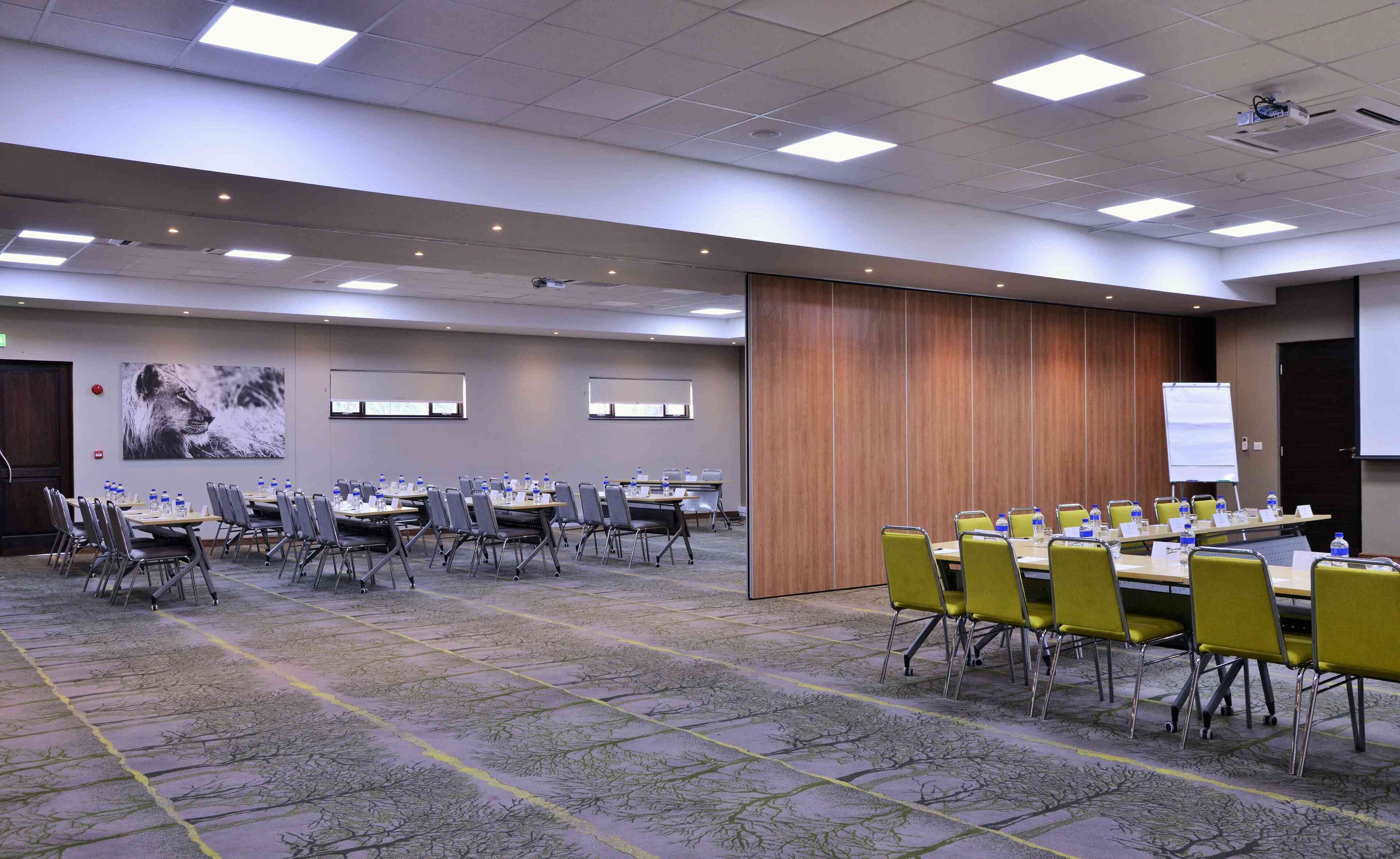 Una sala conferenze con diversi tavoli e sedie, un proiettore e un grande schermo.