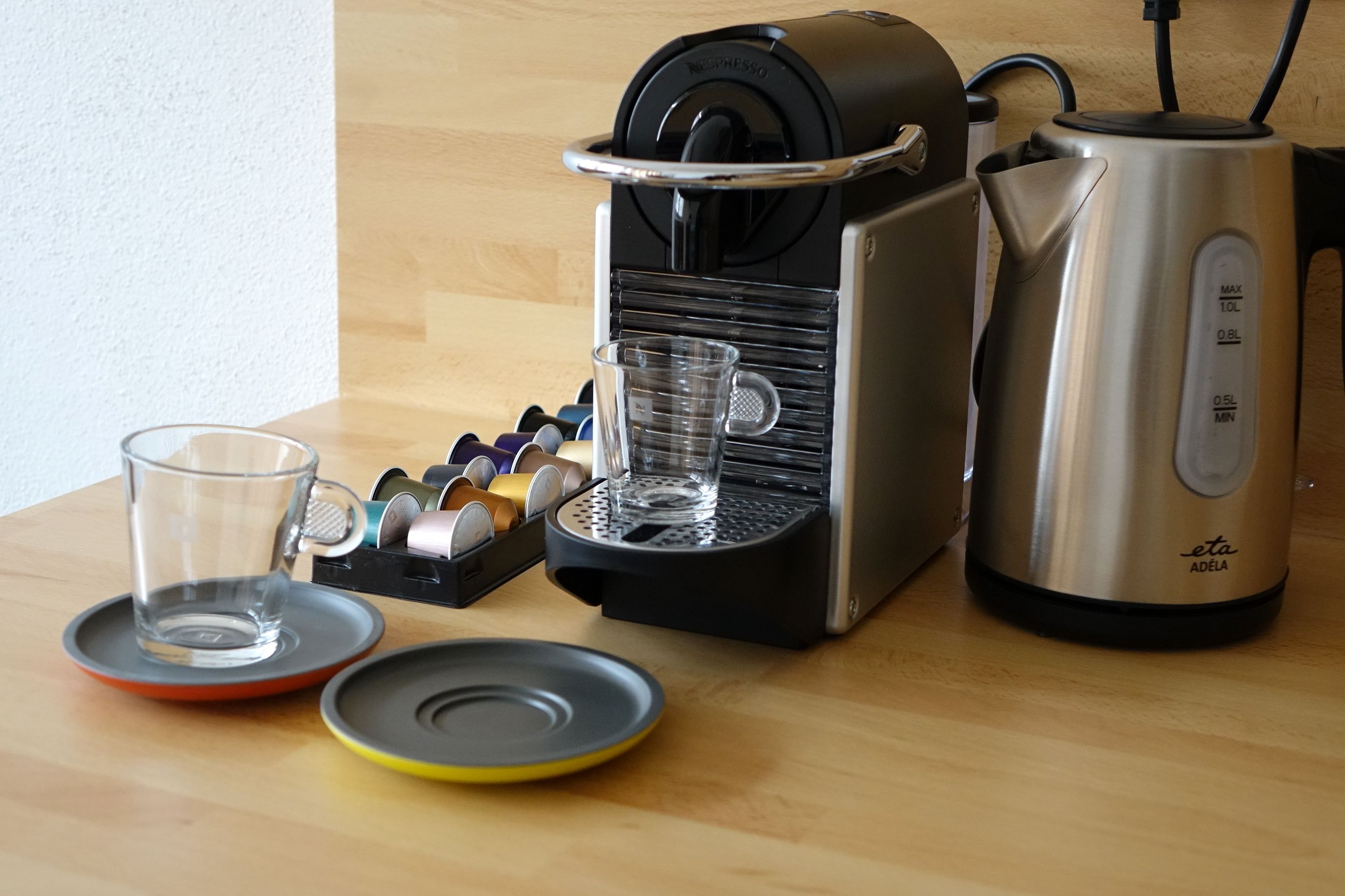 A coffee machine, a glass, and a kettle on a wooden table.