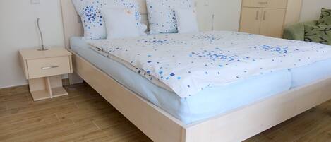 A neatly made bed with a patterned bedspread, a bedside table with a lamp, and a wooden wardrobe in a clean, minimalistic room.